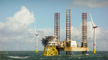 Epische Randansicht auf Große Offshore 8MW Windkraftanlagen, Windpark auf dem Horizont in der Nordsee mit Jack-up-Boot und Offshore-Plattform in welligem Meer