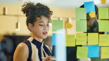 A man and a woman are standing in front of a glass wall writing on sticky notes.