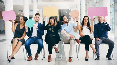 Gruppe von Geschäftsleuten, die bunte Sprechblasen halten, während sie in einem modernen Büro warten