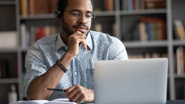 A young man sits in front of his laptop and learns German. 