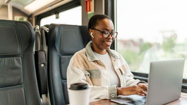Junge afrikanische Geschäftsfrau, die im Zug an ihrem Laptop arbeitet.