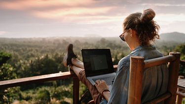 Junge Geschäftsfrau arbeitet mit Laptop auf einer Terrasse mit Blick auf die Berge.