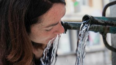Eine Frau trinkt sauberes Wetter aus einem öffentlichen Brunnen