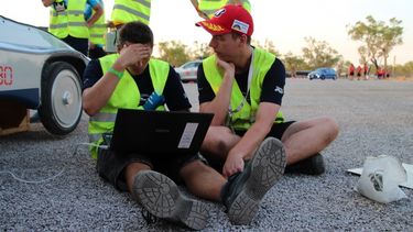 Zwei Ingeneure mit Computer sitzen vor einem Elektromobil und suchen nach einer Lösung für ein technisches Problem