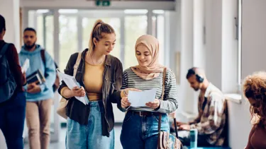 Two female students going through lecture notes as they walk down the corridor.