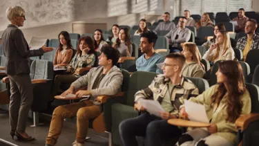 Large group of university students listening to their mature female professor on a class in amphitheater.