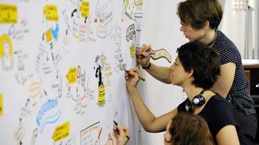 Three women work together on a graphic recording