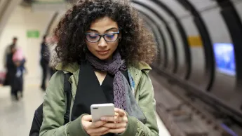 Junge weibliche Pendlerin nutzt ihr Smartphone am Bahngleis in der U-Bahn Station