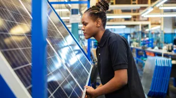 Seitenansicht einer Mitarbeiterin, die neu hergestellte Solarmodule im Unternehmen inspiziert. Weibliche Qualitätsingenieurin, die Sonnenkollektoren in der Fabrik untersucht.