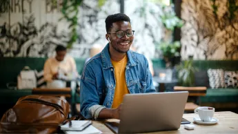 Young man sitting in a café with his laptop and laughing