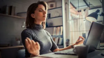 Young woman sitting in meditation pose in front of a laptop