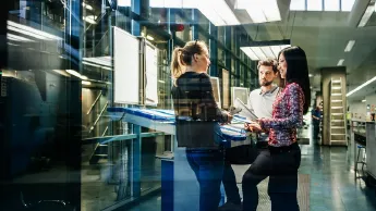 A team of engineers having a discussion at a desk in a large printing factory.