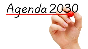 One hand writes "Agenda 2030" with a pen and underlines the words