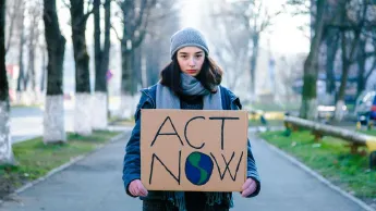 Junge Aktivistin hält Schild gegen Klimawandel "Act now"