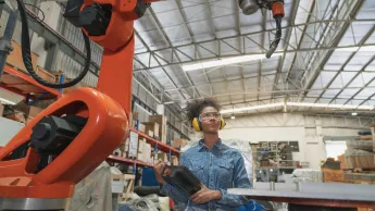 Young African American female engineer operating a robotic welding arm machine in the warehouse factory.