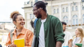 Zwei internationale Studierende gehen zusammen spazieren und plaudern. Im Hintergrund sieht man ein Unigebäude.