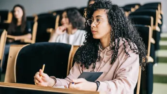 Young woman sits in a lecture, listens attentively and takes notes.