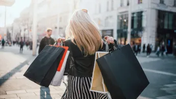 Young woman from behind, holding many shopping bags in her hands.