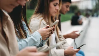 Young adults sit next to each other and look at their smartphones.