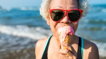 Elderly woman standing on the beach eating an ice cream