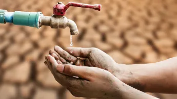 Hands under a dripping tap, a parched desert floor in the background