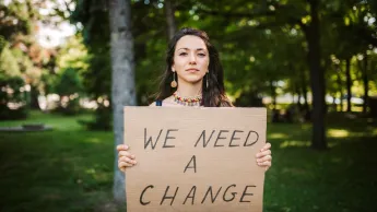 Frau hält Schild "We need a change"