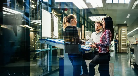 A team of engineers having a discussion at a desk in a large printing factory.