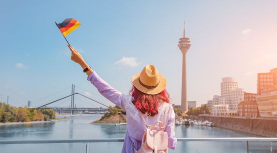 Eine fröhliche asiatische Frau mit deutscher Flagge posiert am Medienhafen und Fernsehturm in Düsseldorf.