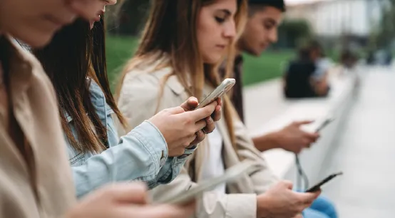 Young adults sit next to each other and look at their smartphones.