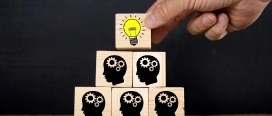 Male hand places a cube with a light bulb on a stack of cubes with gears